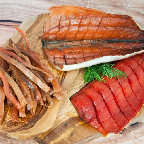 Wildlachs gedörrt Set – Draufsicht auf geräucherten Wildlachs, Filetstreifen und Rotlachsfilet auf Holzbrett